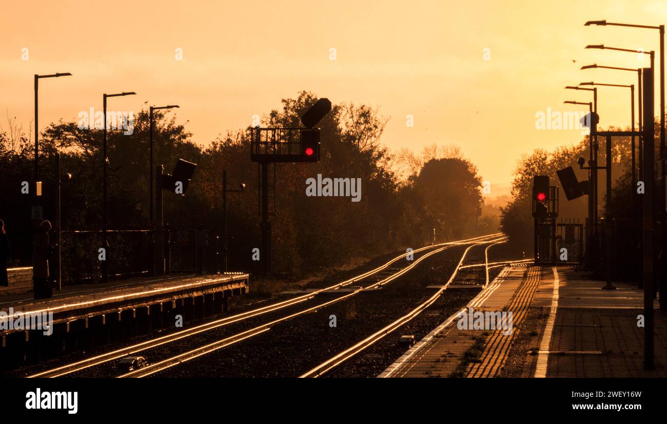 Lever de soleil à la gare ferroviaire de Bicester North sur la ligne principale Chiltern avec le soleil doré qui jaillit de la ligne de chemin de fer avec des signaux lumineux de couleur. Banque D'Images