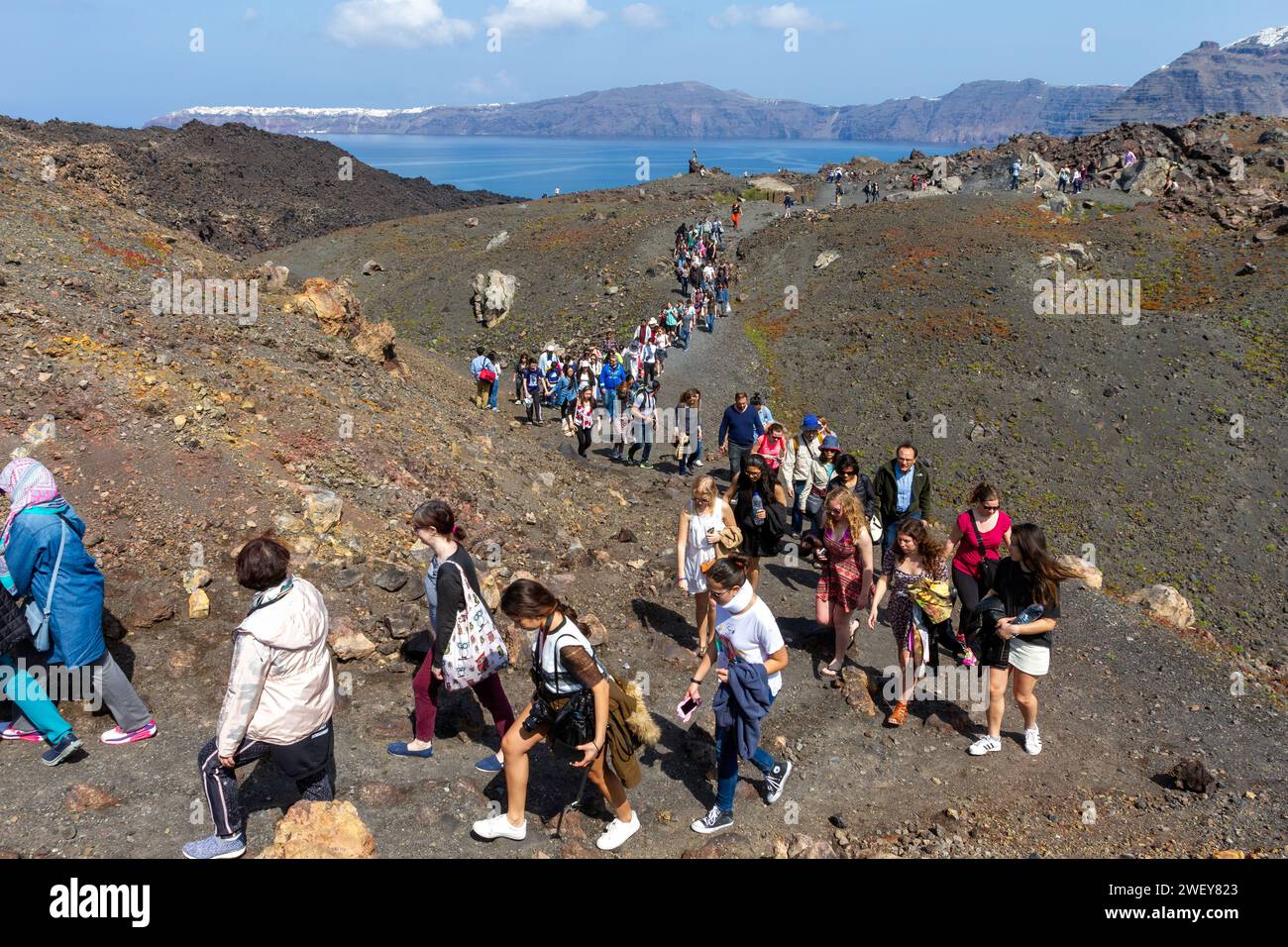 Touristes randonnant sur le volcan actif de l'île de Santorin, en Grèce. À l'arrière-plan, il y a le village pittoresque d'Oia. Banque D'Images