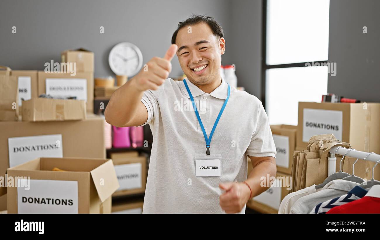 Confiant jeune homme chinois, souriant serviteur montrant le geste pouce-vers-le-haut dans le centre de charité, incarnant l'esprit de volontariat et d'altruisme i. Banque D'Images