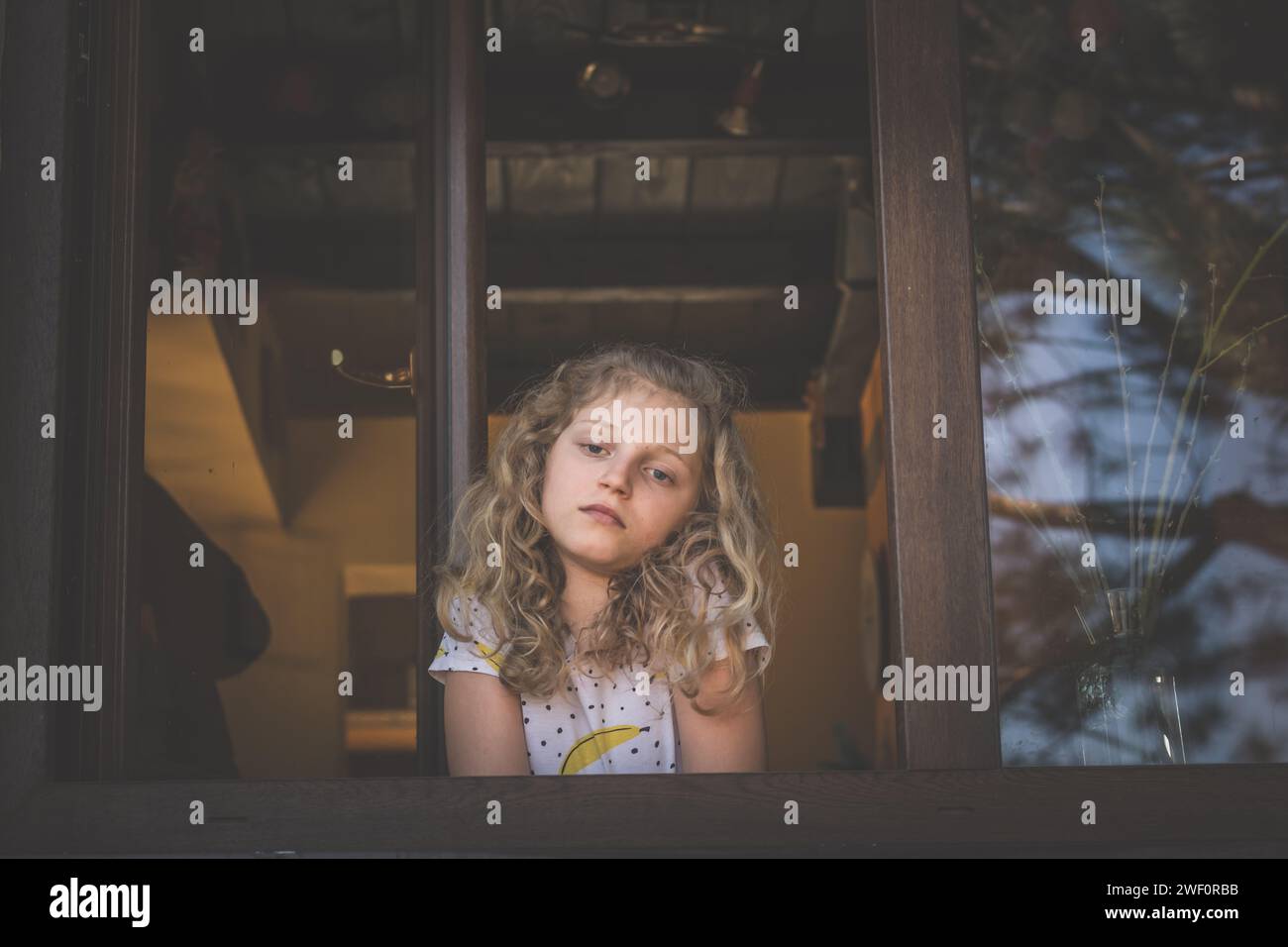 adorable fille avec de longs cheveux blonds regardant par la fenêtre Banque D'Images