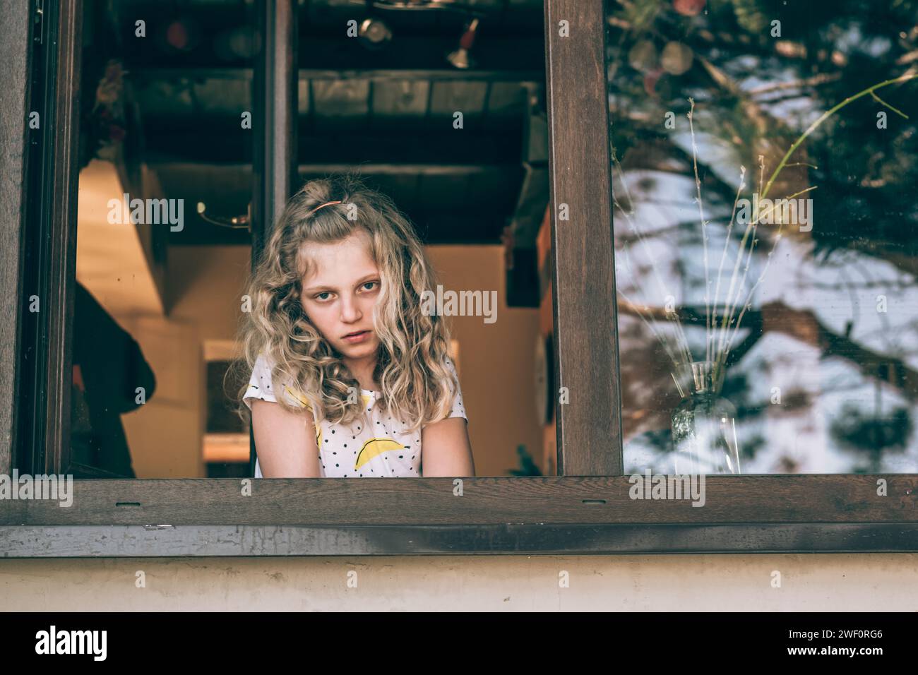 adorable fille avec de longs cheveux blonds regardant par la fenêtre Banque D'Images