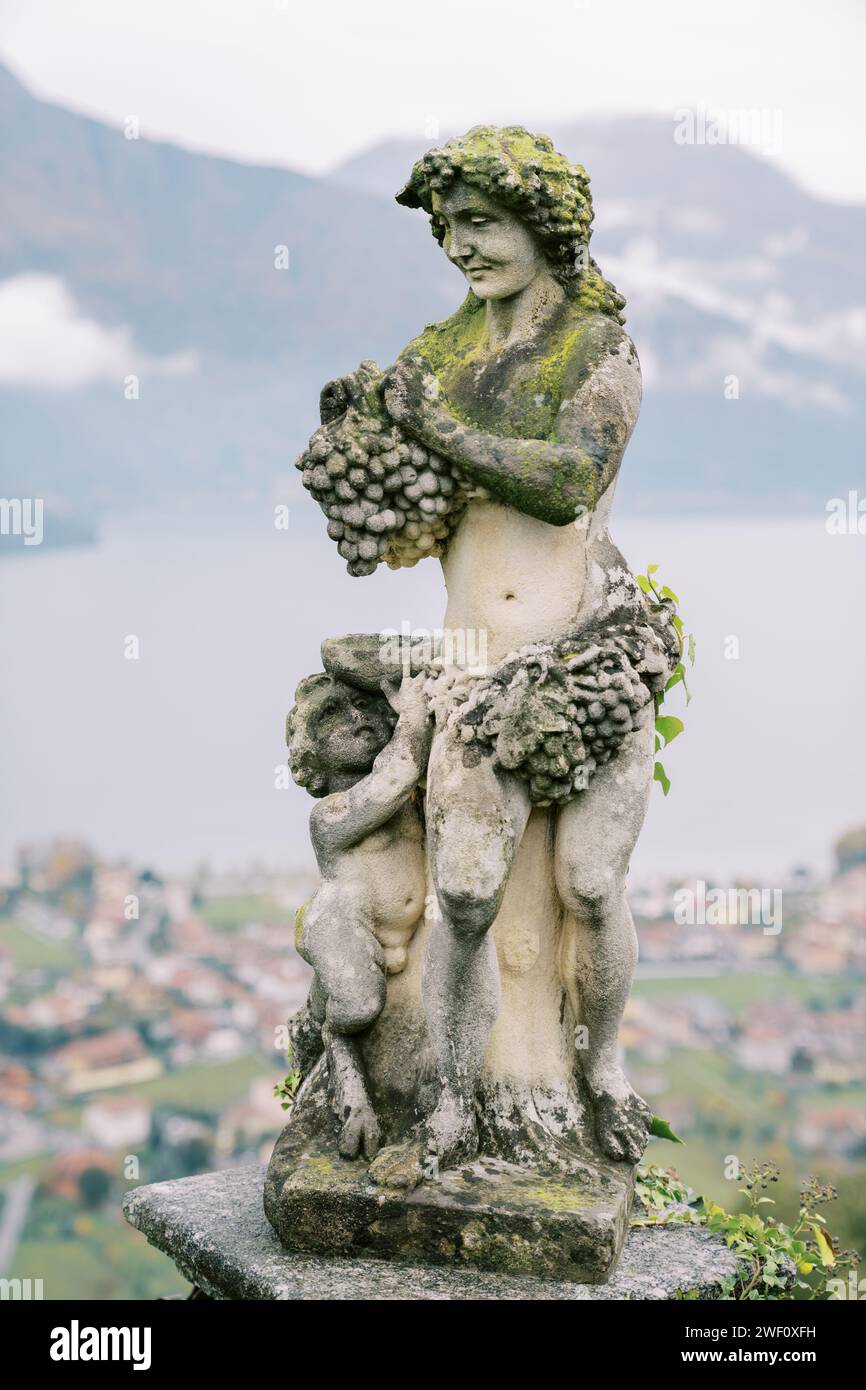 Statue antique de l'ancien dieu grec Dionysos avec une grappe de raisins avec un petit faune avec un bol dans le jardin Banque D'Images