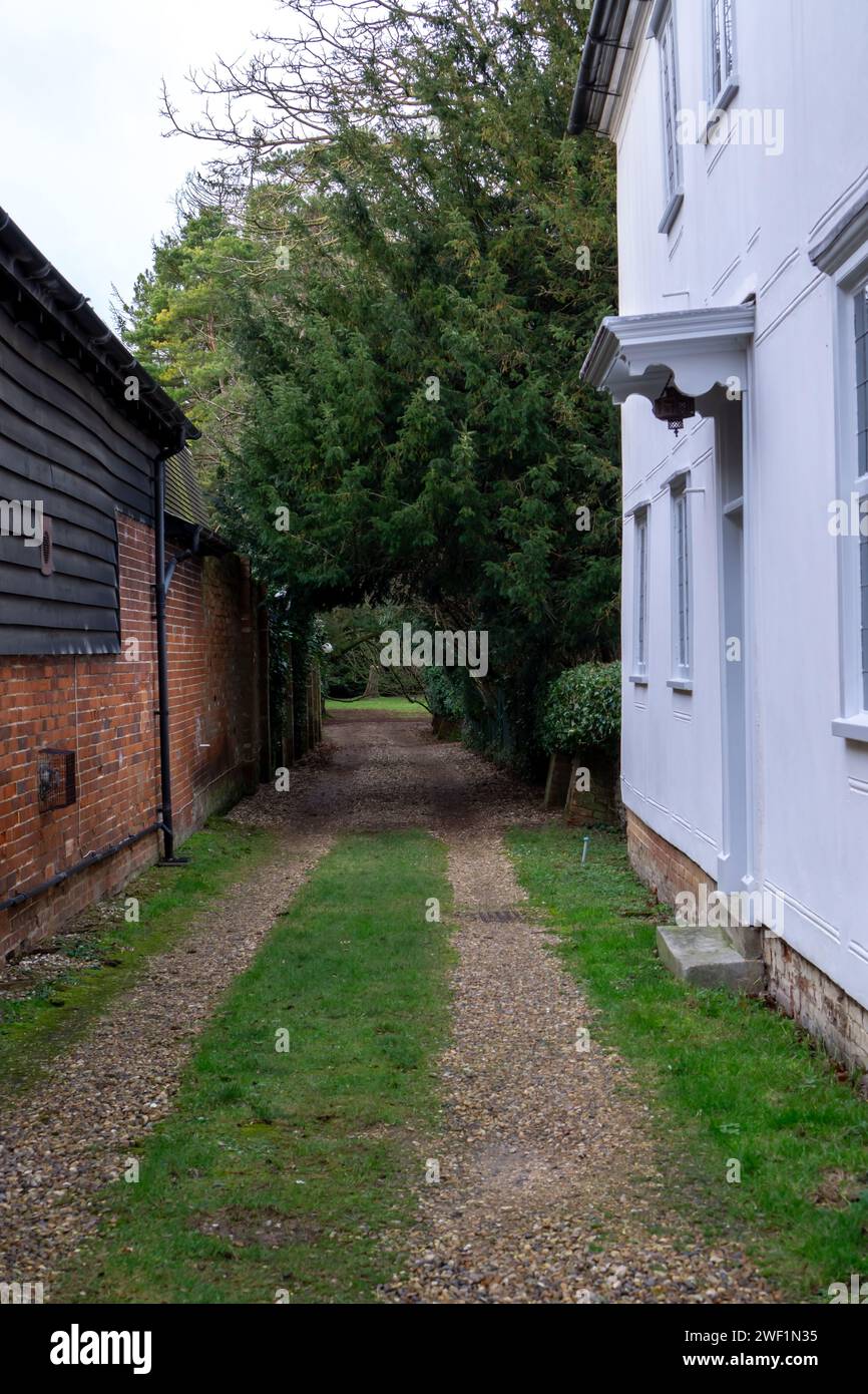 Chemin de gravier avec des arbres formant une entrée voûtée à un champ derrière de vieux bâtiments Banque D'Images