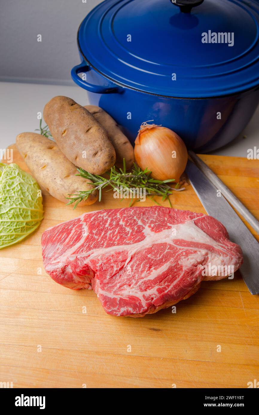 Rôti de bœuf sur une planche à découper en bois avec un couteau et de l'acier aiguisé. pommes de terre, chou, oignon et romarin. Banque D'Images