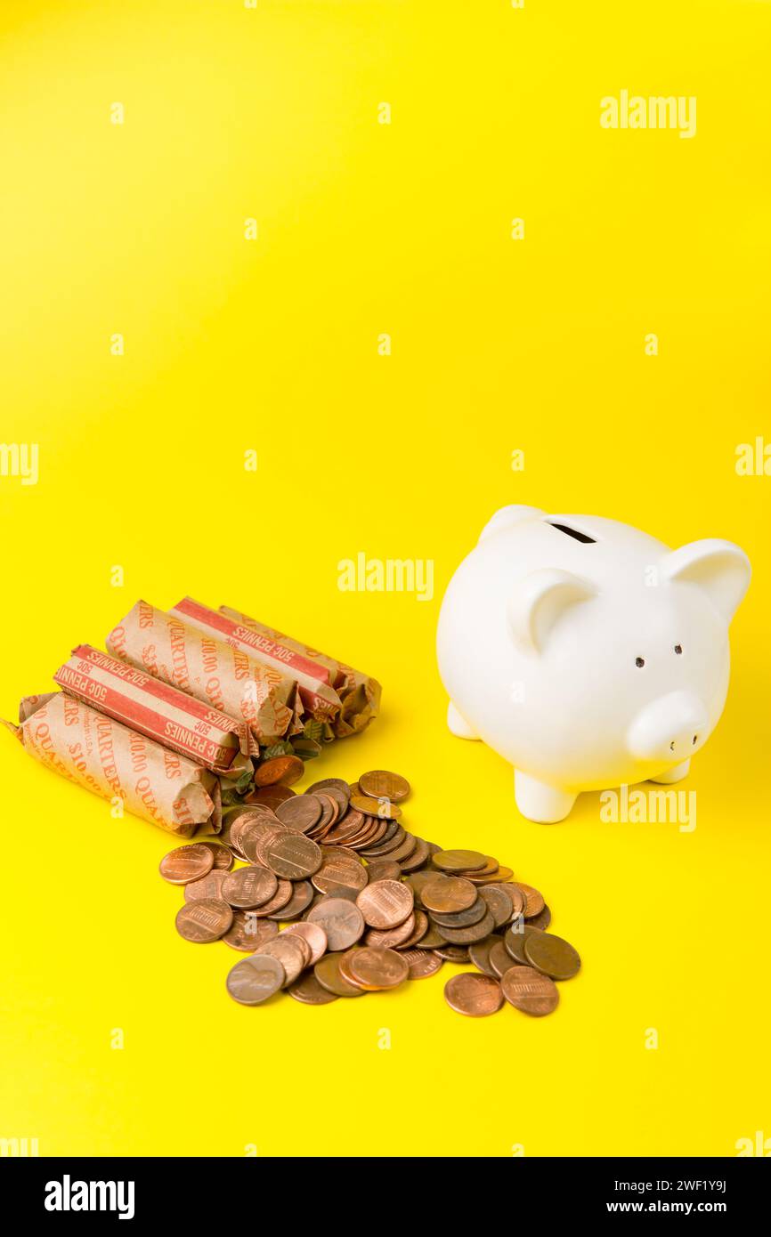Rouleaux de pièces de monnaie américains avec une tirelire blanche sur un fond jaune Banque D'Images