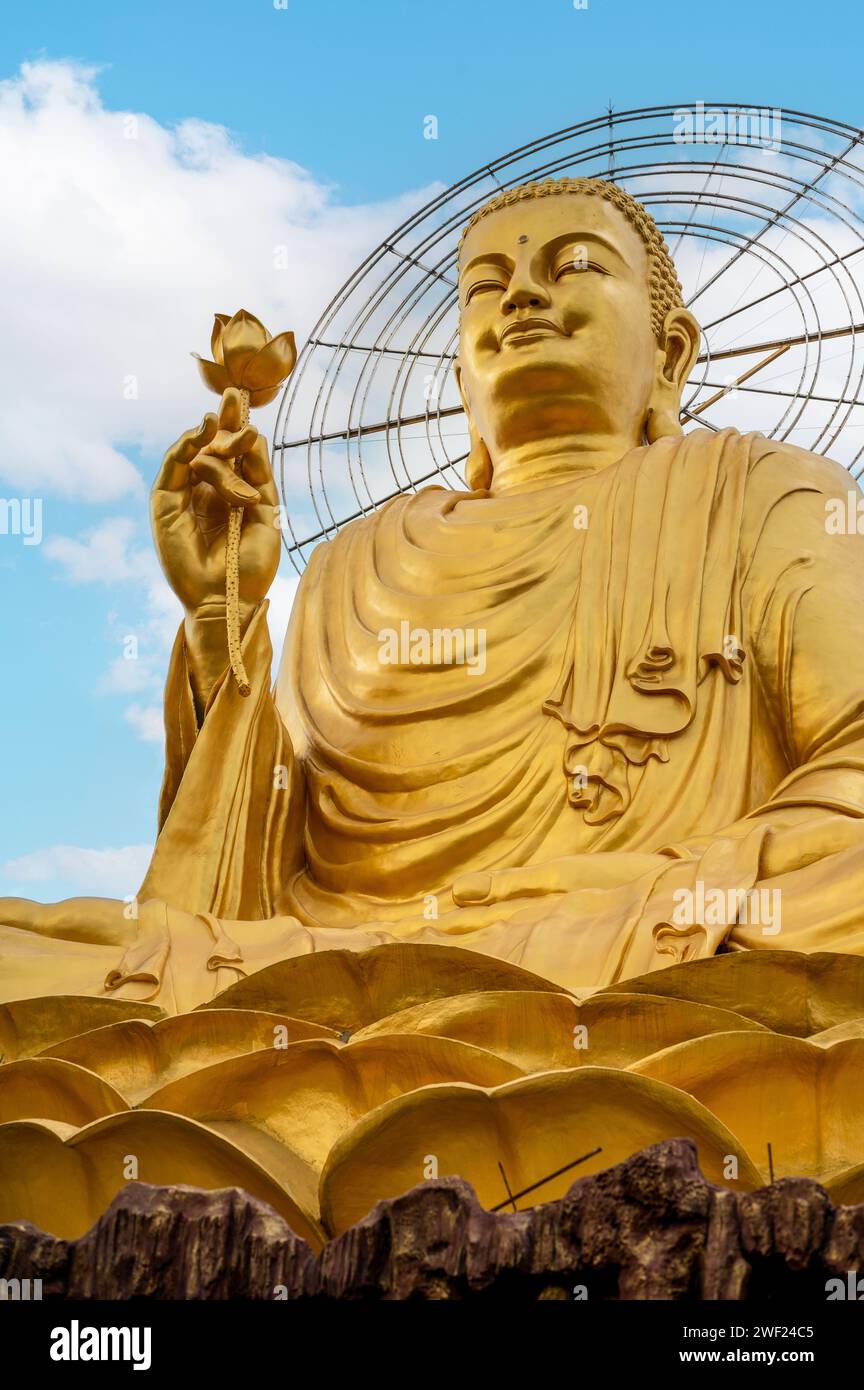 Contre un ciel époustouflant, la majestueuse sculpture de Bouddha doré tient le lotus, exhalant la tranquillité et la signification, symbolisant l'illumination et la paix intérieure. v Banque D'Images
