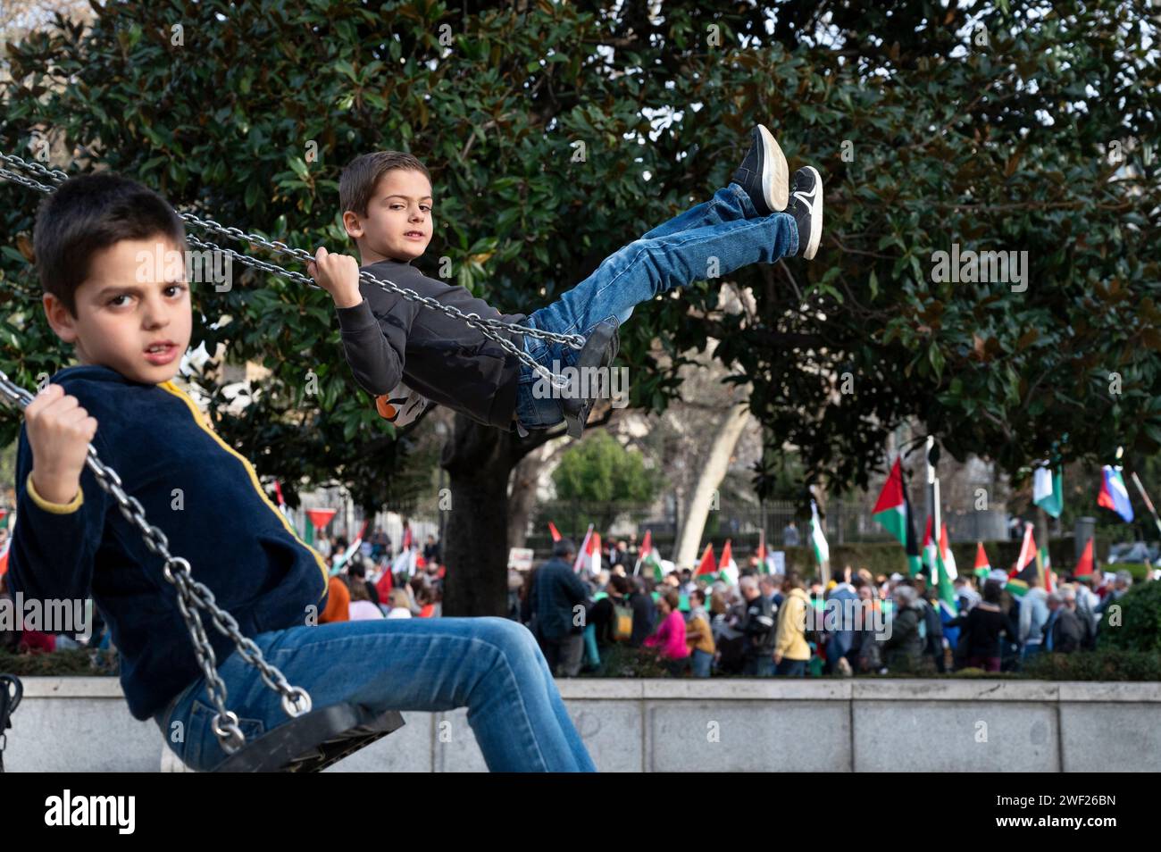 Madrid, Espagne. 27 janvier 2024. Des enfants se balancent devant une aire de jeux alors que les manifestants défilent en solidarité pour la Palestine. L'Assemblée de Madrid avec manifestation en Palestine, sur le thème "Stop au génocide", a vu les voix passionnées de nombreuses personnes unies pour une cause commune contre l'injustice. Crédit : SOPA Images Limited/Alamy Live News Banque D'Images