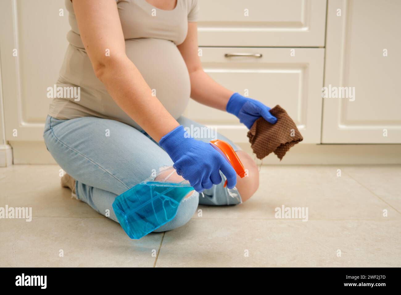 La femme enceinte fait des travaux ménagers dans la cuisine, en utilisant un chiffon pour essuyer le sol. La femme enceinte nettoie la cuisine, assurant hy Banque D'Images