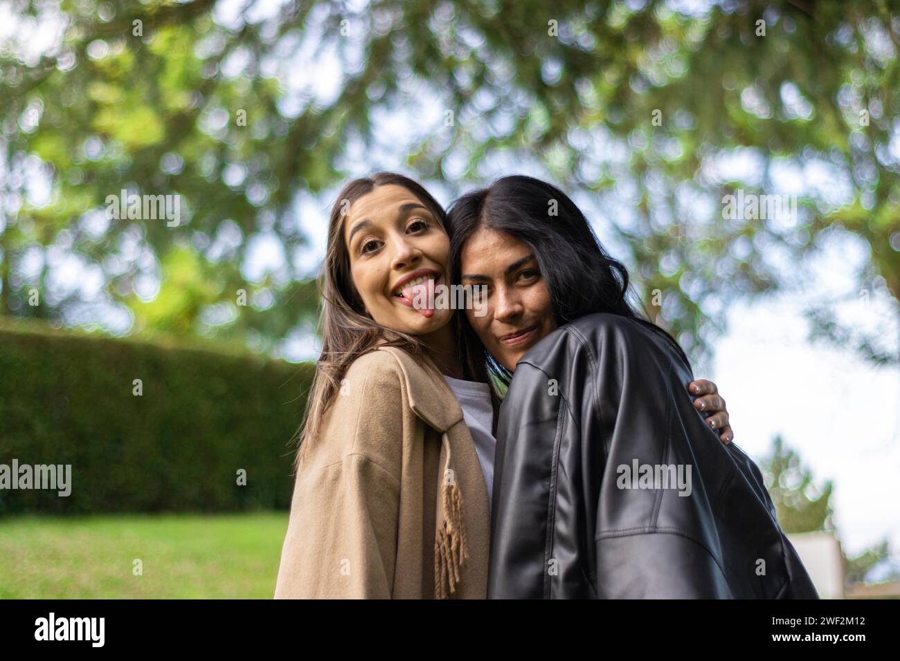 Deux amies ensemble regardant joyeusement la caméra avec des branches d'arbre derrière eux Banque D'Images