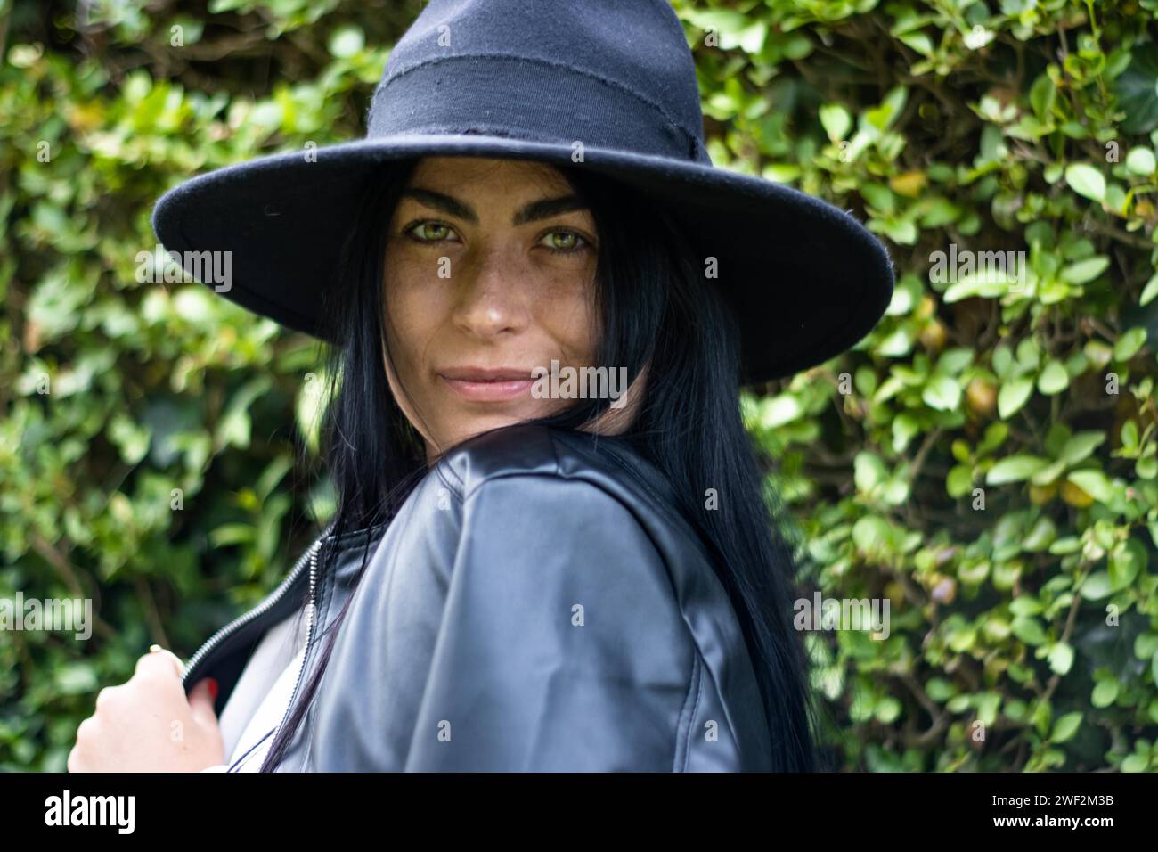 Portrait d'une jeune femme souriante dans un chapeau regardant la caméra avec des feuilles vertes en arrière-plan à l'extérieur Banque D'Images