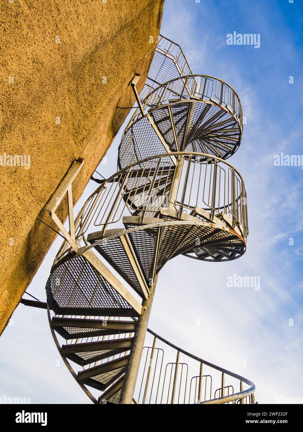 Cette image capture la conception complexe d'un escalier en colimaçon métallique montant le long de l'extérieur d'un bâtiment beige sous un ciel bleu clair. Banque D'Images