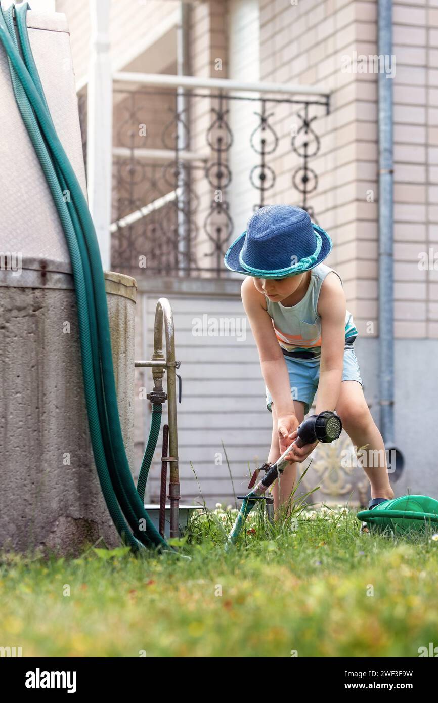 Un petit garçon dans un chapeau bleu au puits, se préparant à arroser le jardin de sa grand-mère. Banque D'Images