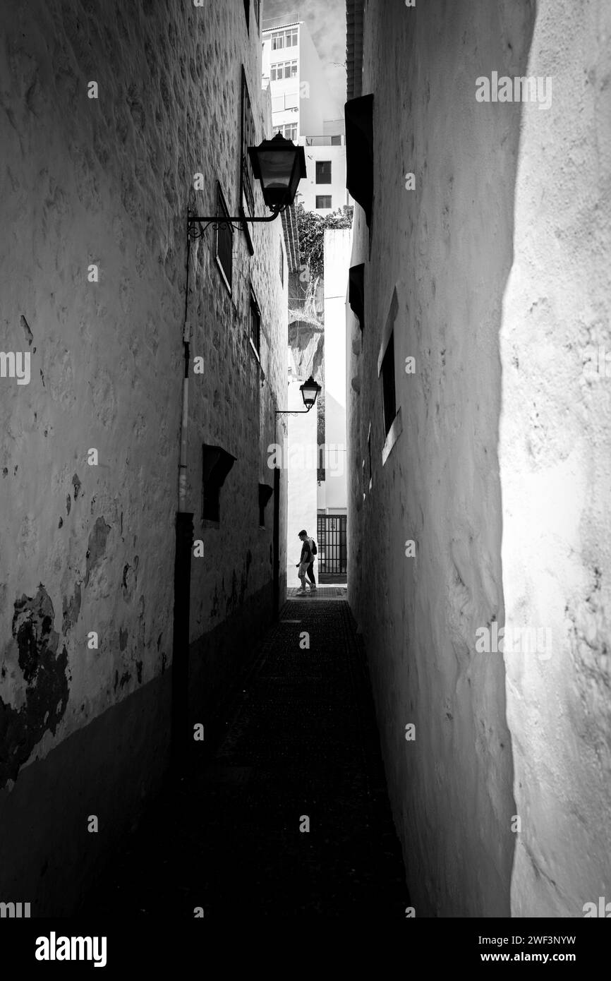 Passage étroit entre les bâtiments rendus peints en blanc avec la personne marchant devant l'extrémité, jour ensoleillé, lumière de rue unique Banque D'Images