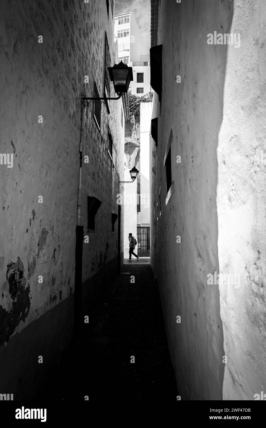 Passage étroit entre les bâtiments rendus peints en blanc avec la personne marchant devant l'extrémité, jour ensoleillé, lumière de rue unique Banque D'Images