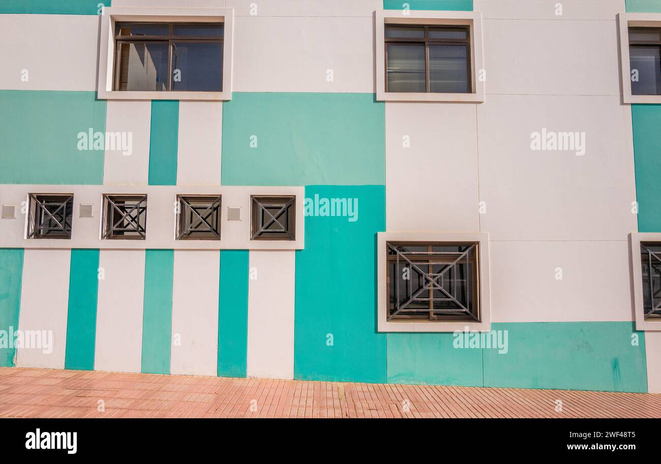 Nuances de rayures vertes peintes sur un bâtiment moderne et fenêtres carrées et grilles de sécurité en métal. Banque D'Images