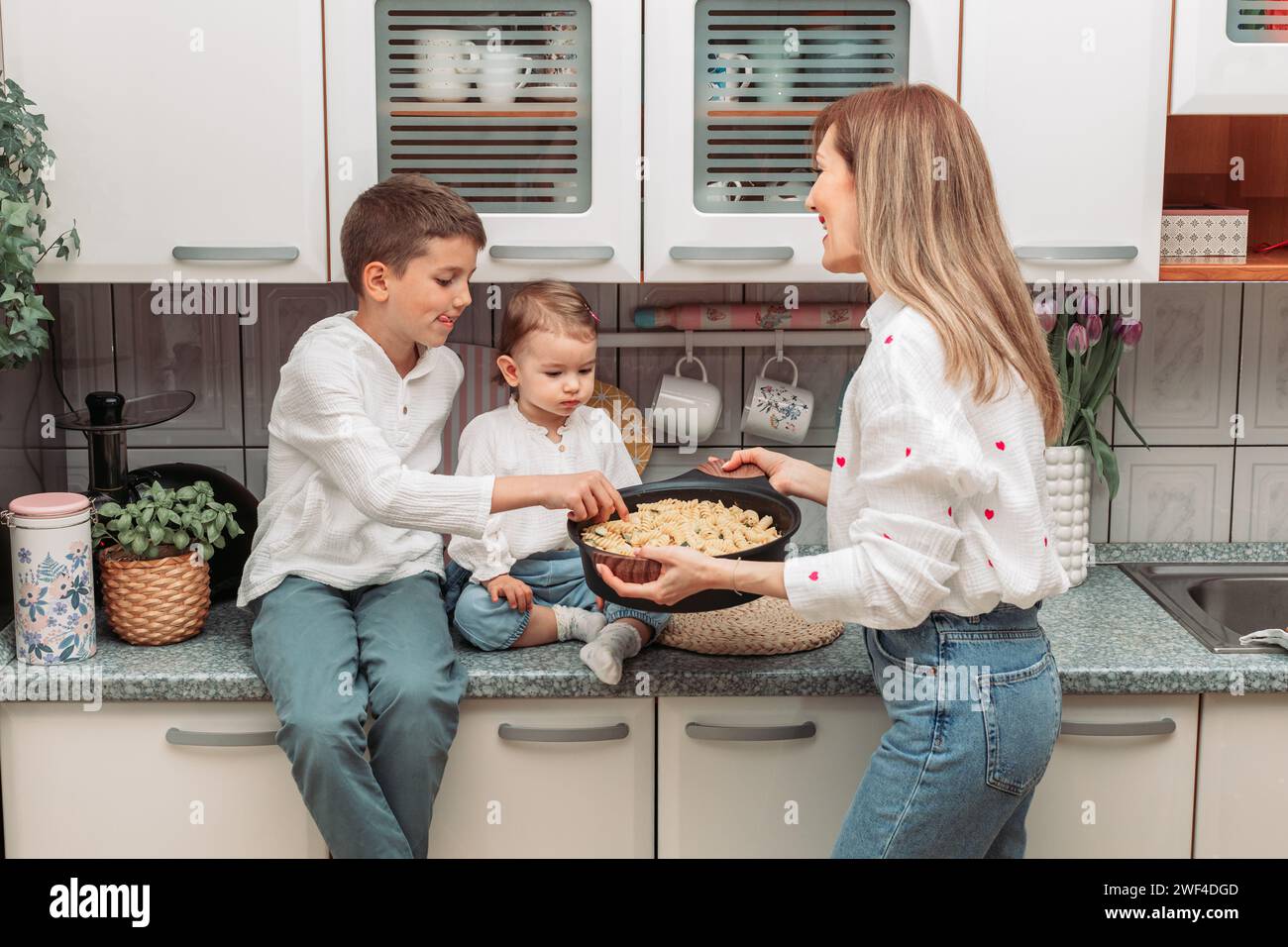 Maman et ses enfants dans la cuisine avec des pâtes dans la casserole pour le dîner Banque D'Images