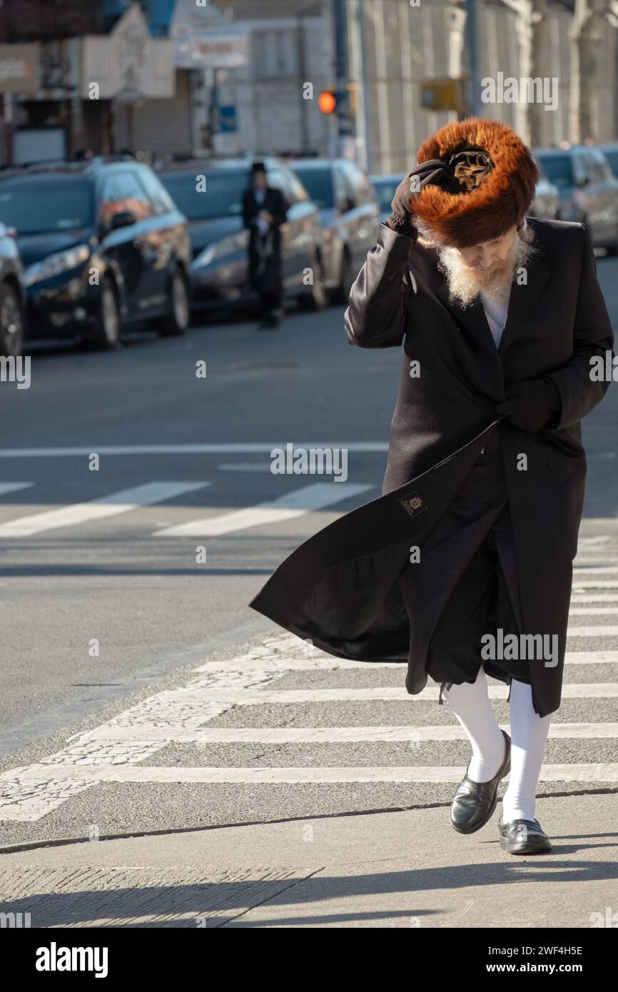 Sur Pourim 2023 un homme juif orthodoxe marche dans le vent tout en tenant son chapeau de fourrure shreimel. À Williamsburg, Brooklyn, New York. Banque D'Images