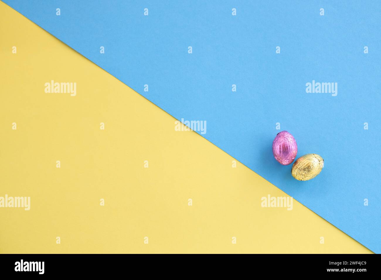 Vue de dessus des oeufs de Pâques en chocolat rose et or sur fond diagonal jaune et bleu Banque D'Images