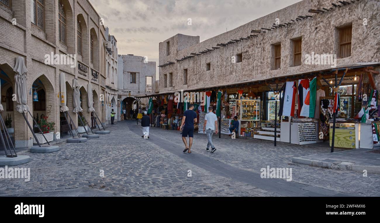 Souq Waqif à Doha, Qatar rue principale au coucher du soleil lors de la coupe asiatique AFC 2023 montrant magasin de textile arabe, cafés et habitants et visiteurs marchant. Banque D'Images