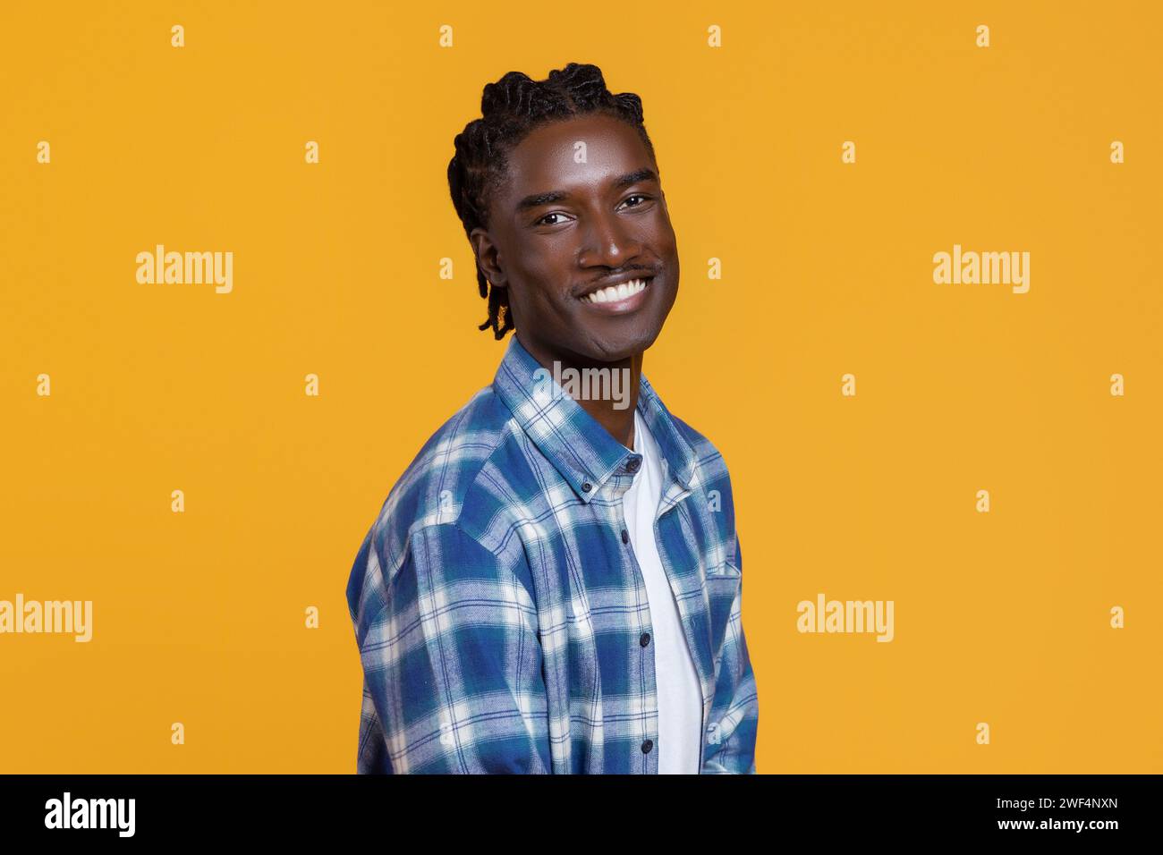 Beau jeune homme noir avec les cheveux tressés debout à moitié tourné sur fond jaune Banque D'Images