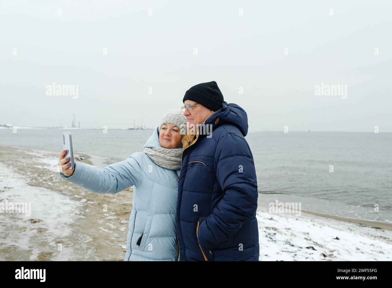 Portrait d'un couple de personnes âgées profitant d'une promenade hivernale sur la plage, prenant un selfie. Banque D'Images