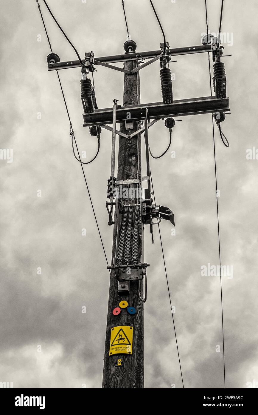 Un poteau de ligne aérienne rurale de 11 kV contre un ciel couvert, montrant les identificateurs de trois phases colorés et l'avis de danger. Comté de Durham, Royaume-Uni. Banque D'Images