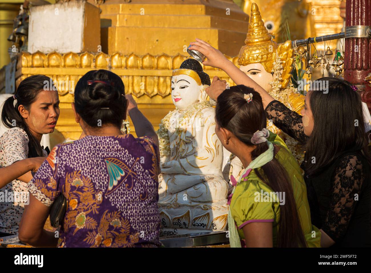 Groupe de femmes locales versant de l'eau sur une statue de Bouddha à la pagode Shwedagon à Yangon, Myanmar, un matin ensoleillé. Banque D'Images