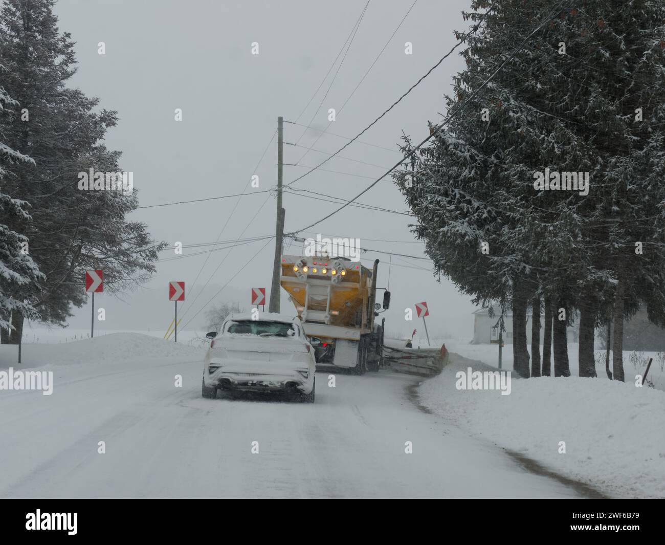 Voiture suivant un camion chasse-neige déneigeant une route. Québec, Canada Banque D'Images