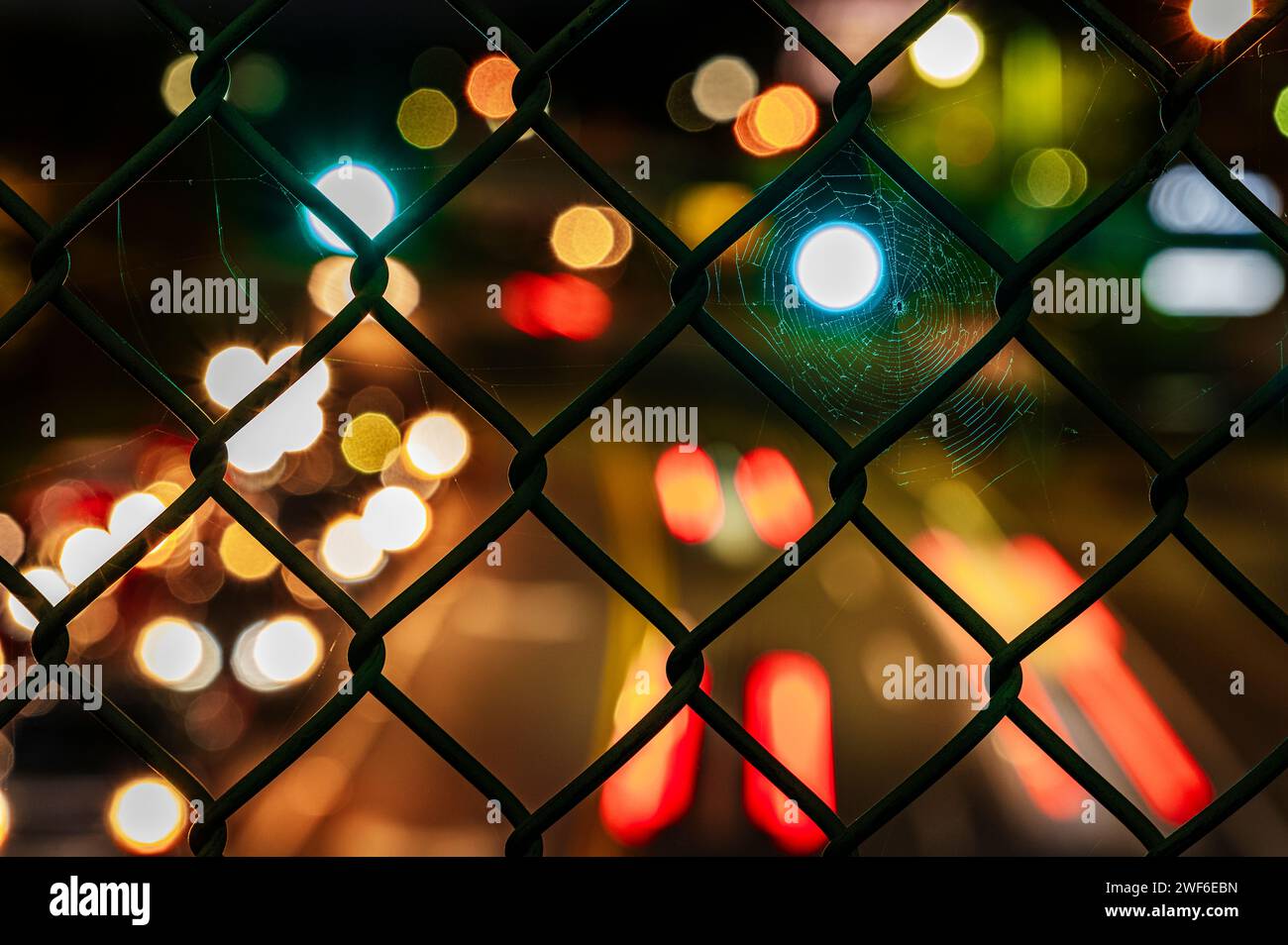 Vue rapprochée d'une clôture à maillons avec un effet bokeh envoûtant des lumières de la ville floues dans l'arrière-plan nocturne. Banque D'Images