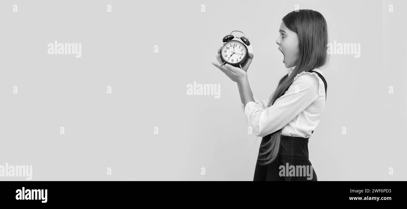 jeune fille choquée dans l'uniforme de l'école avec réveil montrant l'heure sur fond jaune, ponctualité. Enfant adolescent avec réveil, poste horizontal Banque D'Images