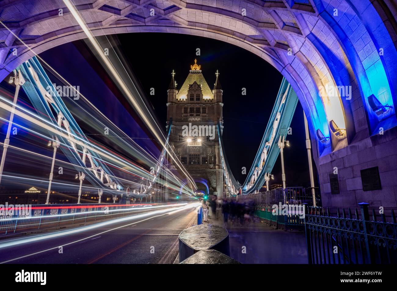 Une nuit, longue exposition photographiée sur Tower Bridge avec des piétons, des touristes visitant ce monument emblématique et des sentiers légers de passage des véhicules. Banque D'Images