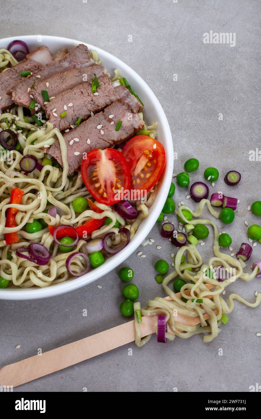 Nouilles Ramen aux épinards et au chou frisé avec oignon de printemps, pois et tranches de bœuf sur gris tacheté avec espace de copie Banque D'Images