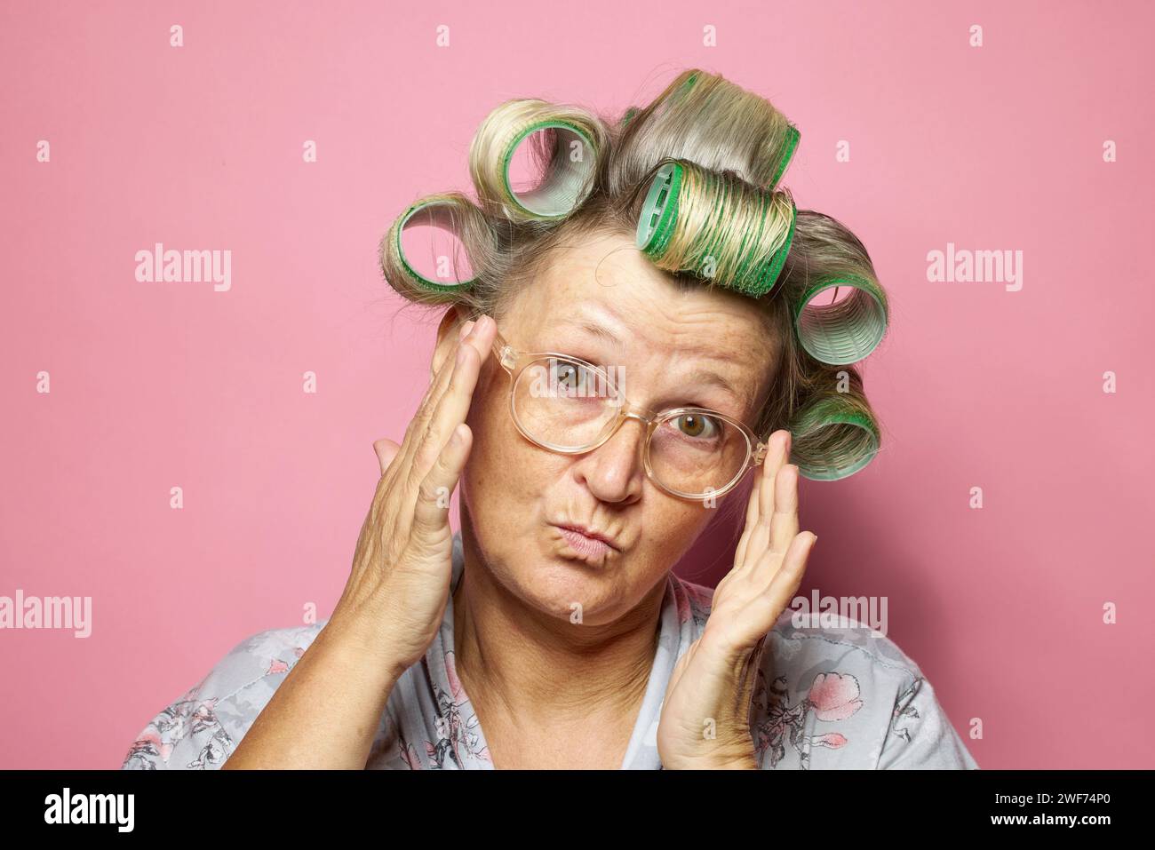 drôle étonné surpris les femmes âgées avec des rouleaux de cheveux et des lunettes sur fond rose Banque D'Images