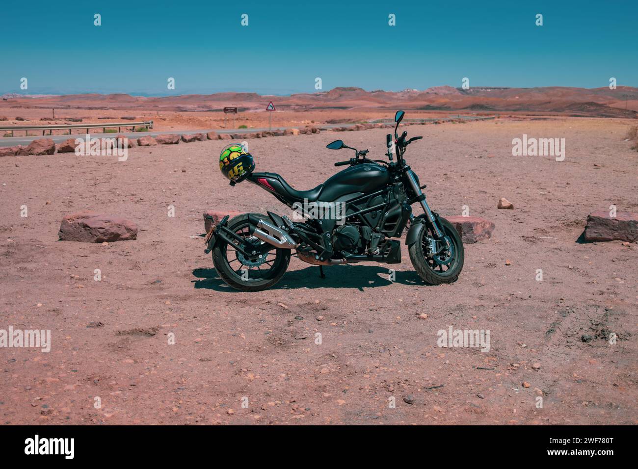 Une moto se dresse sur le terrain accidenté du cratère Ramon, invitant à un voyage aventureux à travers le paysage désertique d'Israël. Banque D'Images