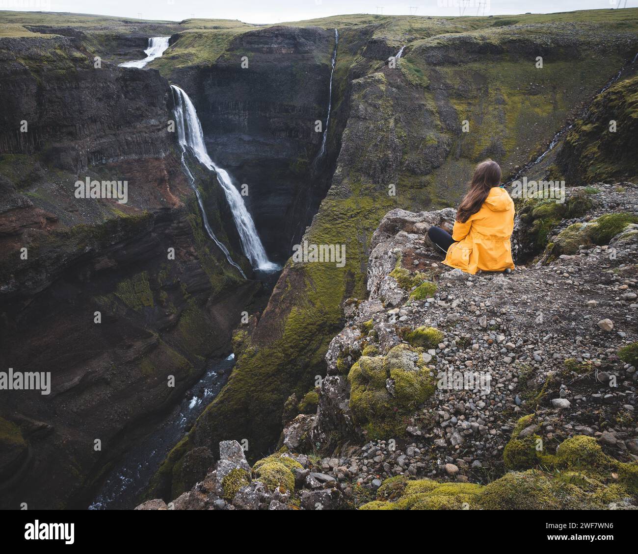 Aventure en Islande : veste de pluie jaune, éperon rocheux et cascade majestueuse Banque D'Images