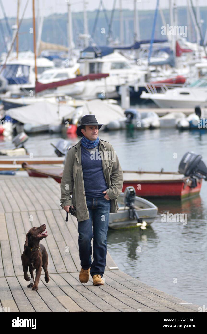 Un homme se promène dans une marina avec son chien adorateur et attentif Banque D'Images