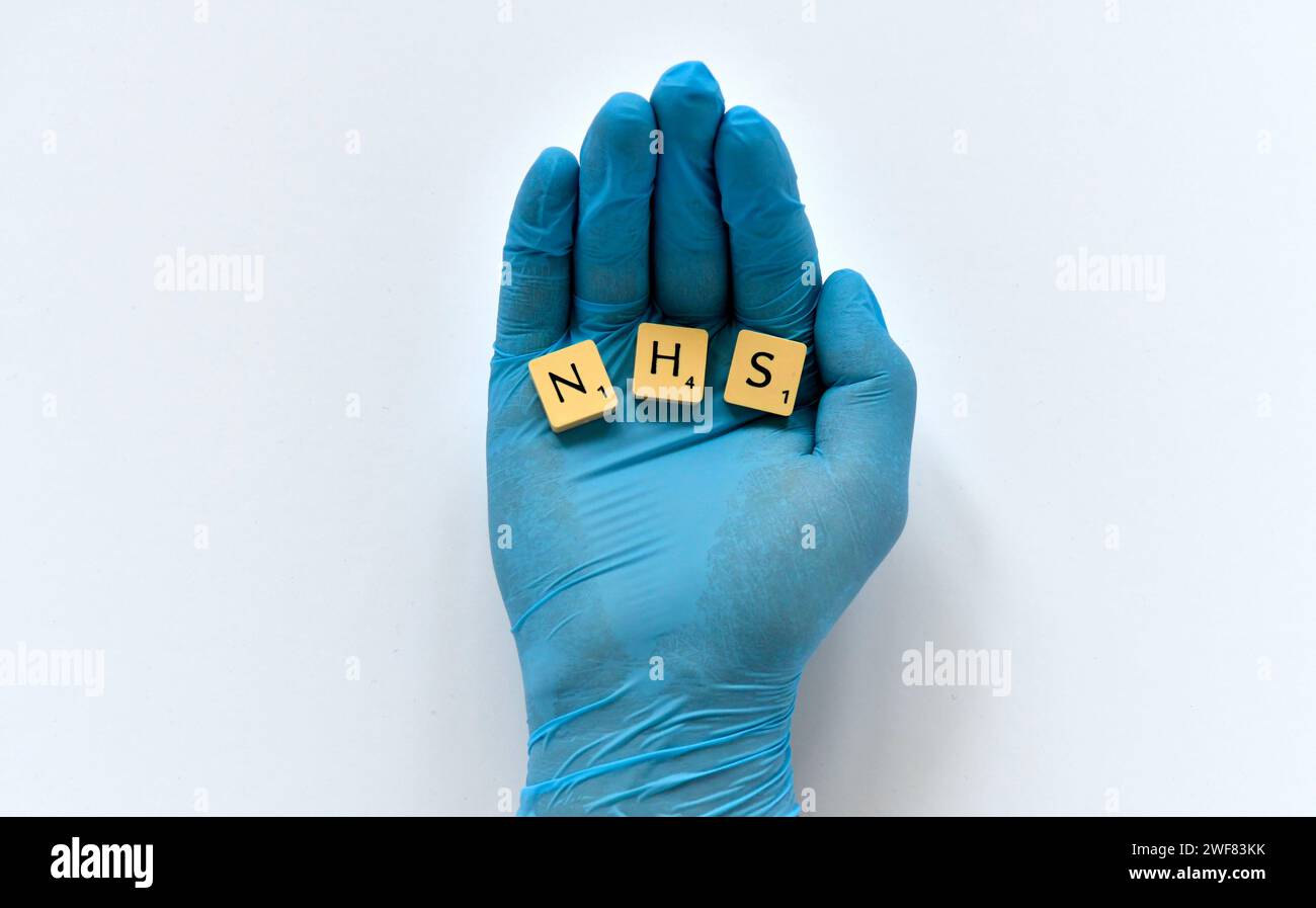 Une main gantée en latex bleu tient trois morceaux de scrabble épelant NHS en lettres. Banque D'Images
