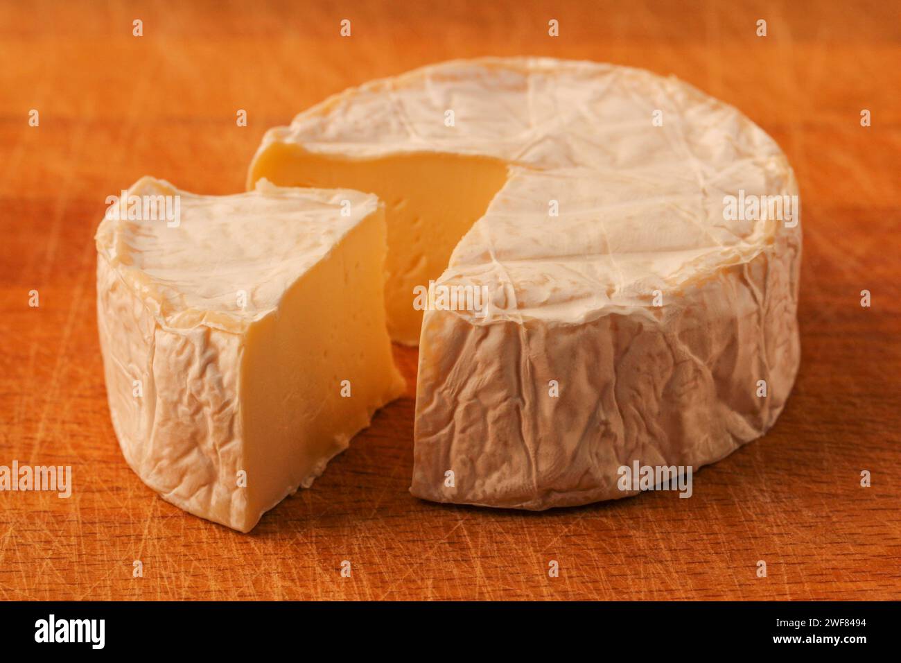 Camembert. Tête de fromage avec un morceau coupé sur une planche à découper en bois Banque D'Images