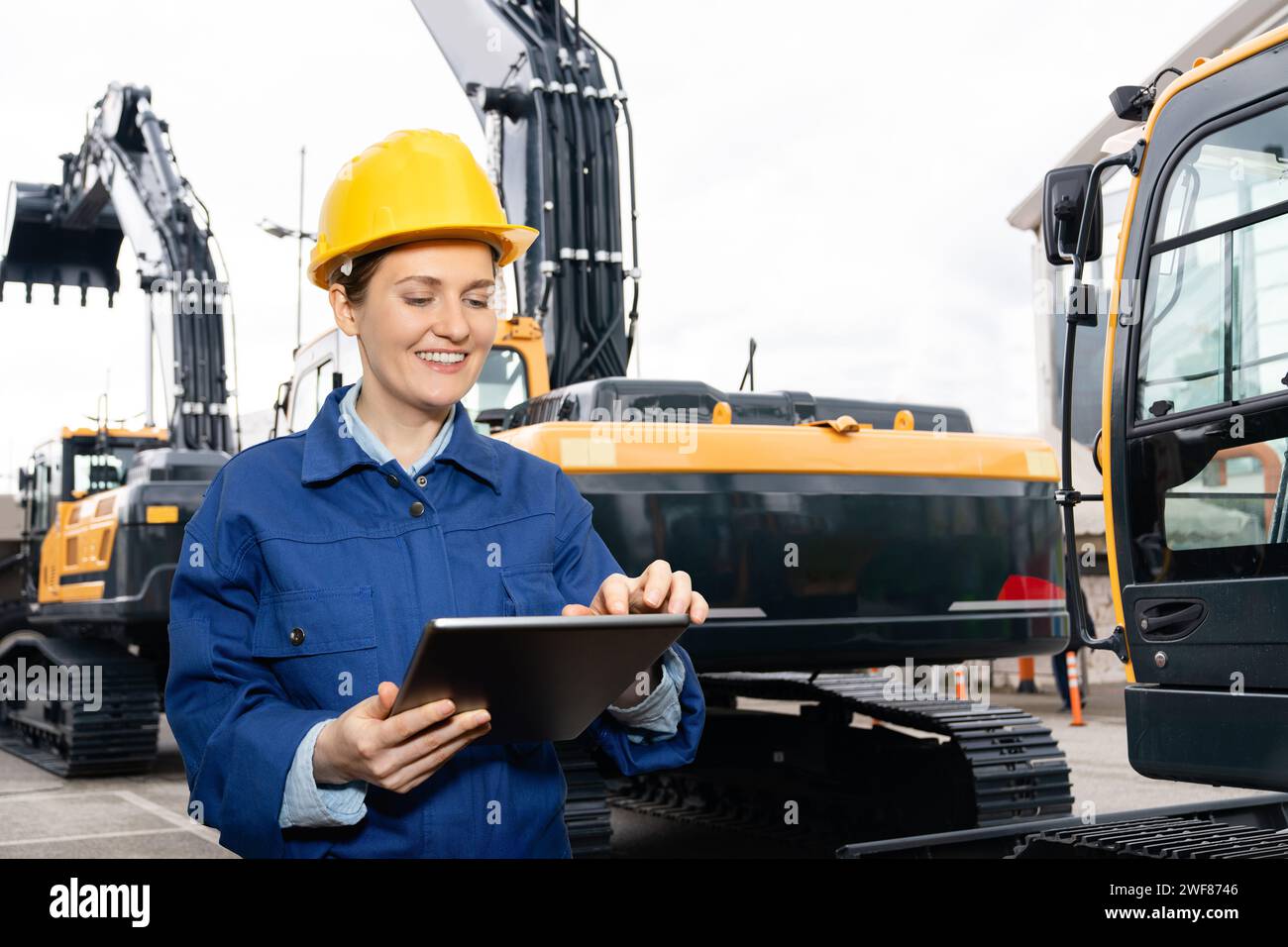 Femme ingénieur dans un casque avec une tablette numérique se tient à côté des pelles de construction. Banque D'Images