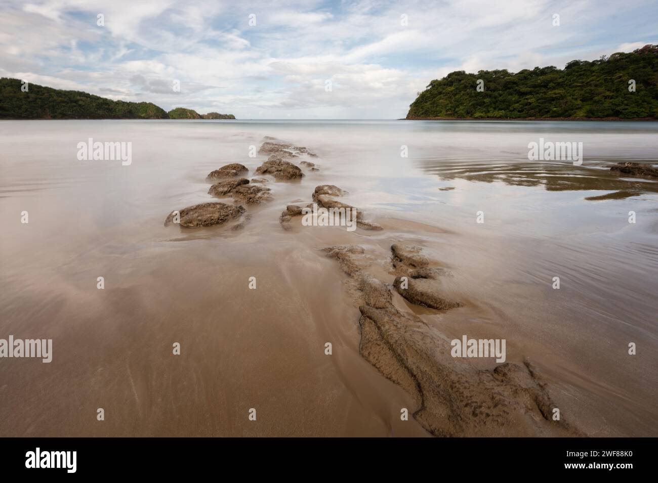 Eau soyeuse sur la baie de plage de l'océan avec rangée de pierres Banque D'Images