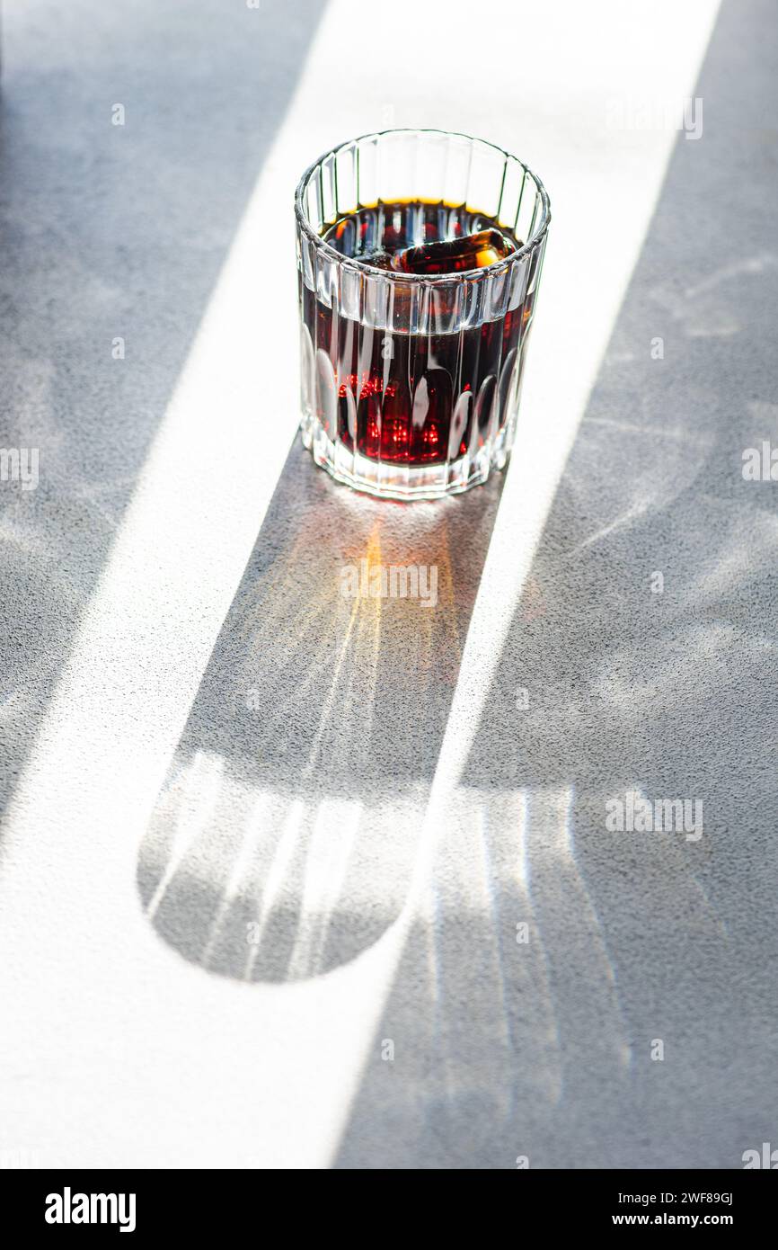 Verre rempli de liqueur de cerise projetant une longue ombre sur une surface texturée éclairée par la lumière du soleil Banque D'Images