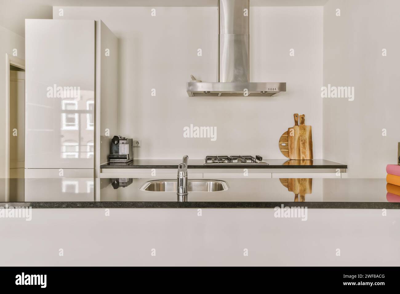 Une cuisine élégante dispose d'une cuisinière en acier inoxydable, d'une hotte et d'un évier, complétés par un design minimaliste d'armoire blanche. Banque D'Images