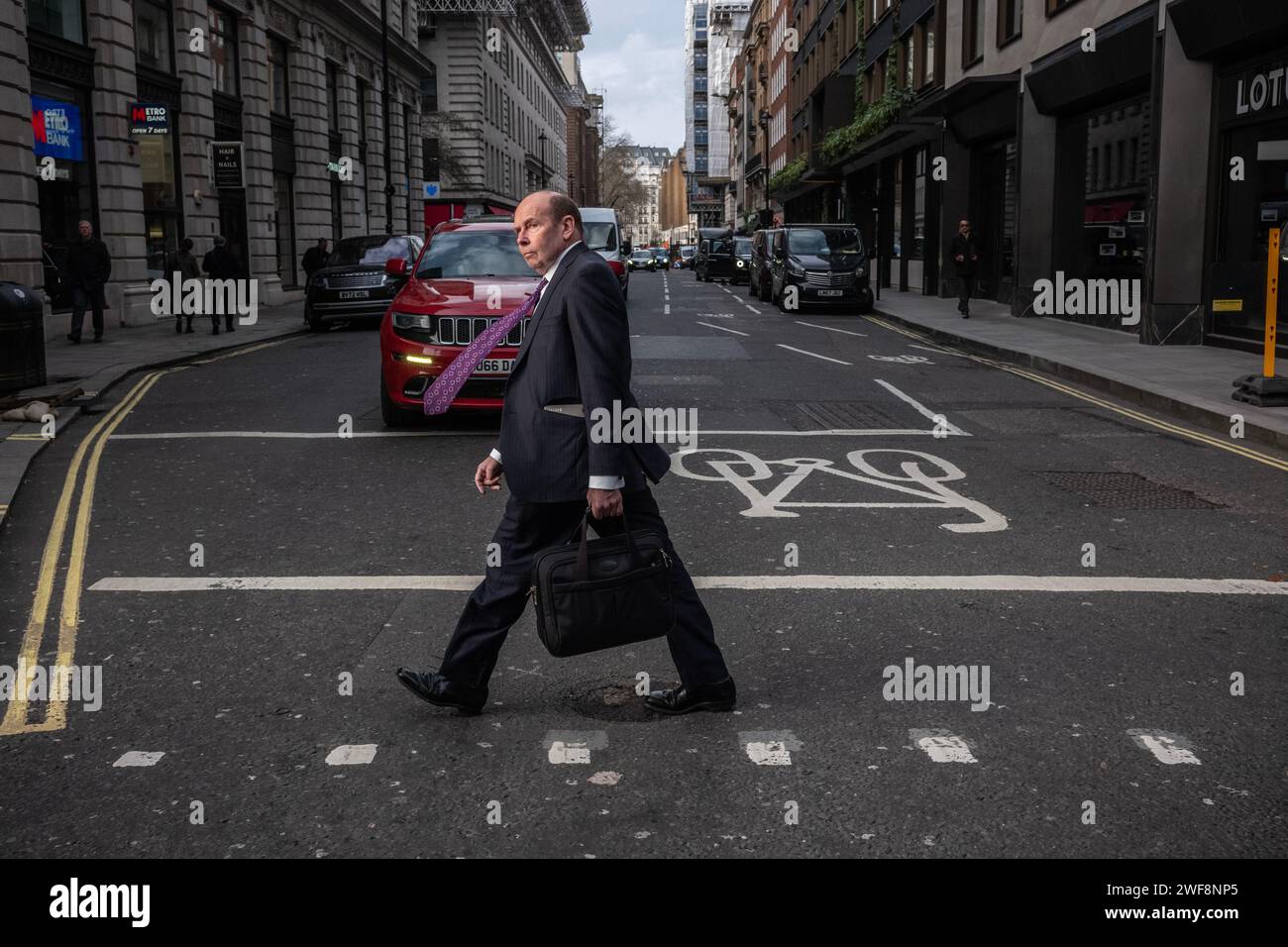 Un homme d'affaires marche le long de Piccadilly à Mayfair tandis que le vent souffle sa cravate de costume violet sur un après-midi d'hiver blustère à Londres, Angleterre, Royaume-Uni Banque D'Images