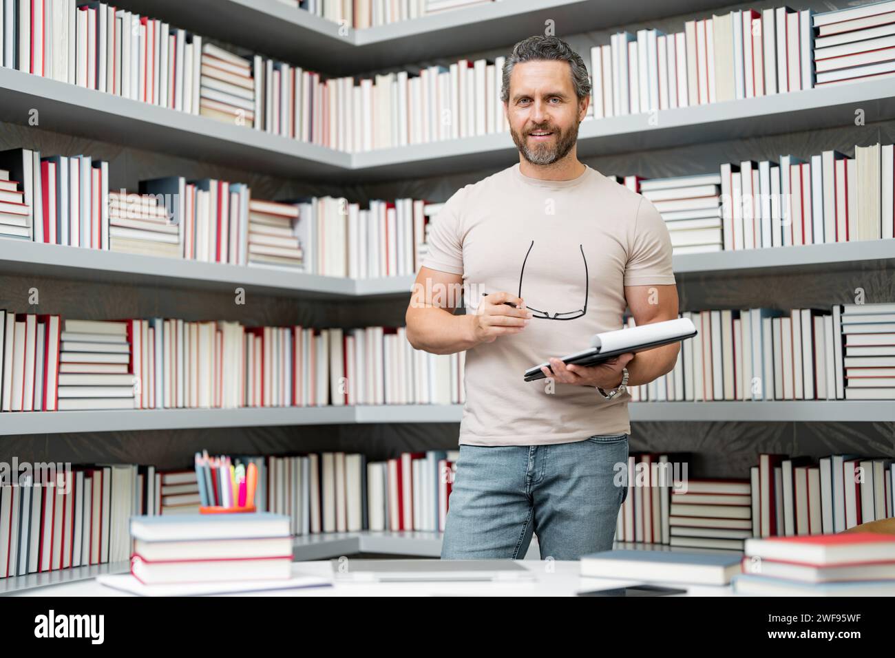 Portrait de l'enseignant dans la salle de classe de la bibliothèque. Beau professeur à la bibliothèque de l'université. Journée des enseignants. Cours de professeur. Professeur d'école à la bibliothèque Banque D'Images