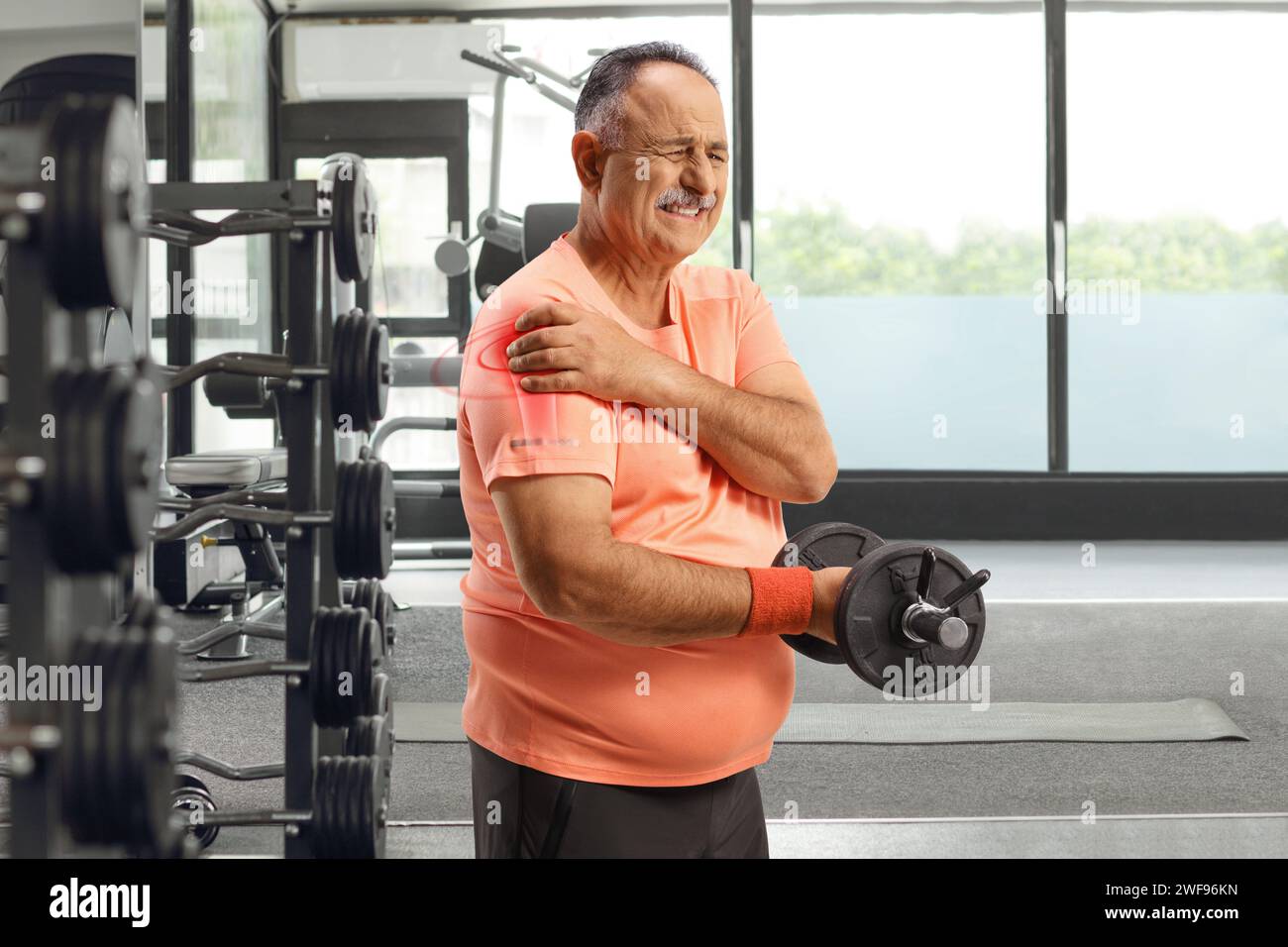 Homme mature à la salle de gym avec une blessure à l'épaule soulevant des poids Banque D'Images