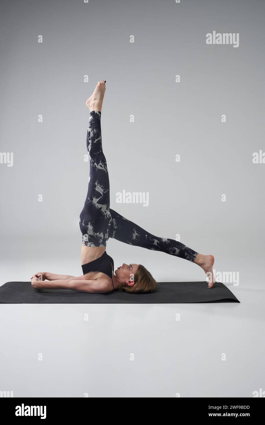 Femme caucasienne sérieuse pratiquant la position de yoga Halasana sur tapis de gymnastique. Vue latérale d'une femme mince aux cheveux clairs dans une tenue de sport s'étirant et se relaxant Banque D'Images Femme caucasienne sérieuse pratiquant la position de yoga Halasana sur tapis de gymnastique. Vue latérale d'une femme mince aux cheveux clairs dans une tenue de sport s'étirant et se relaxant Banque D'Images