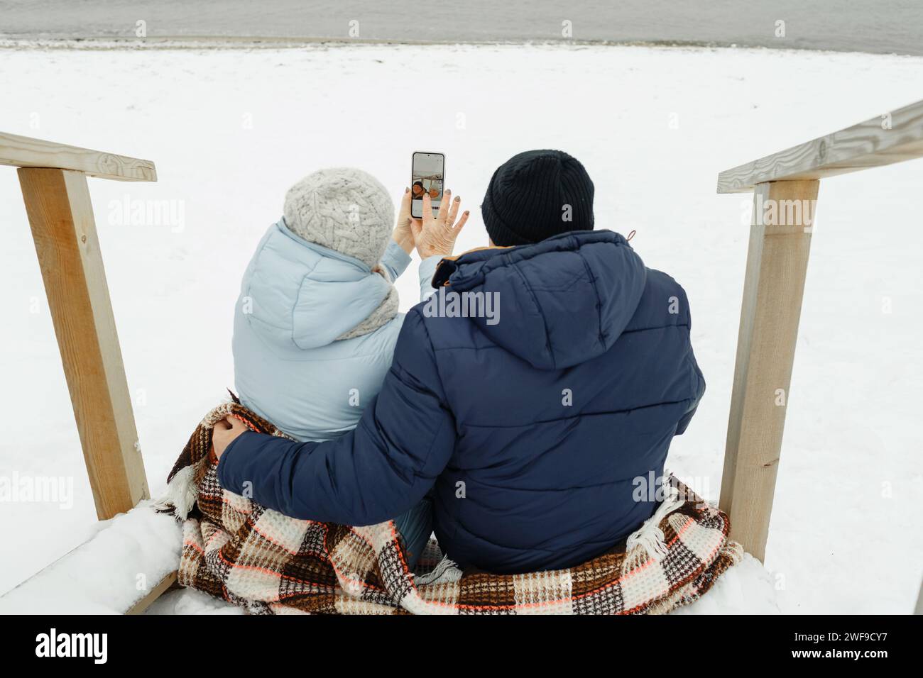 Heureux couple de personnes âgées assis ensemble sur les escaliers au bord de la mer en hiver, prenant un selfie. Banque D'Images