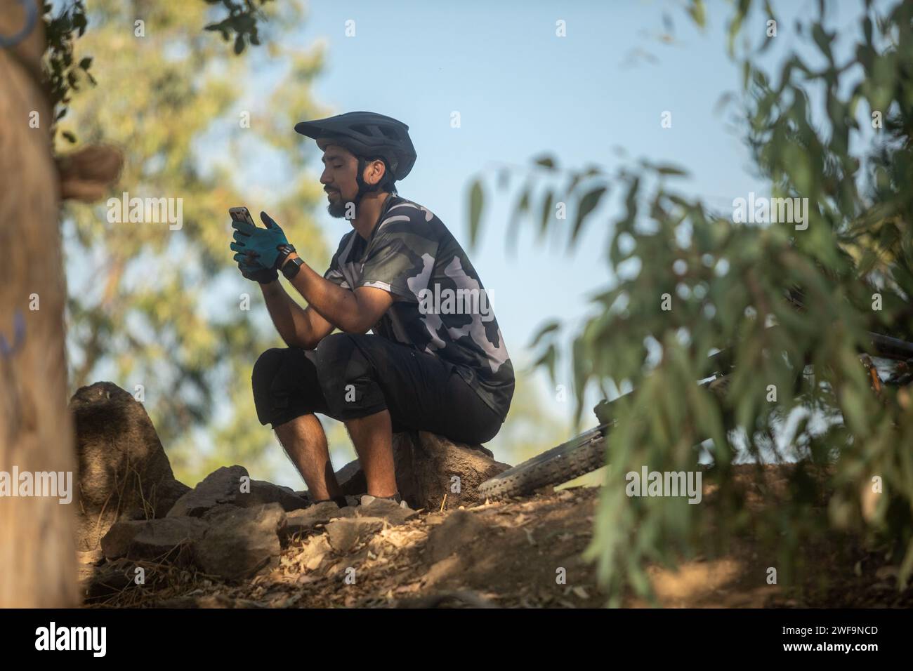 Cycliste masculin latino vérifiant son téléphone assis sur un rocher Banque D'Images