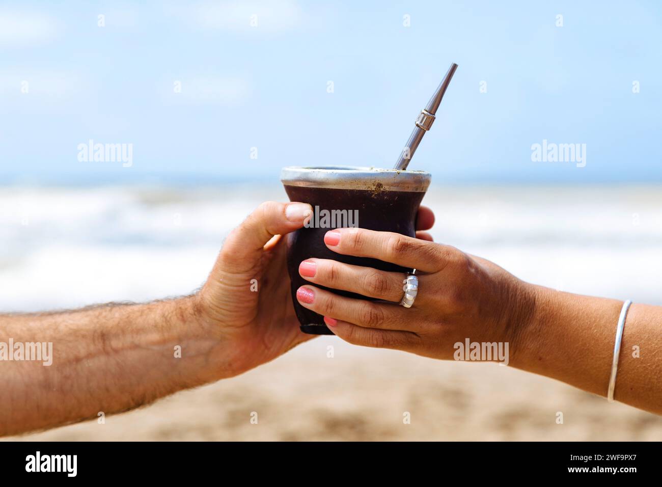 Femme donnant à un homme une boisson chaude Yerba Mate sur la plage. Couple ou amis partageant Mate. Banque D'Images
