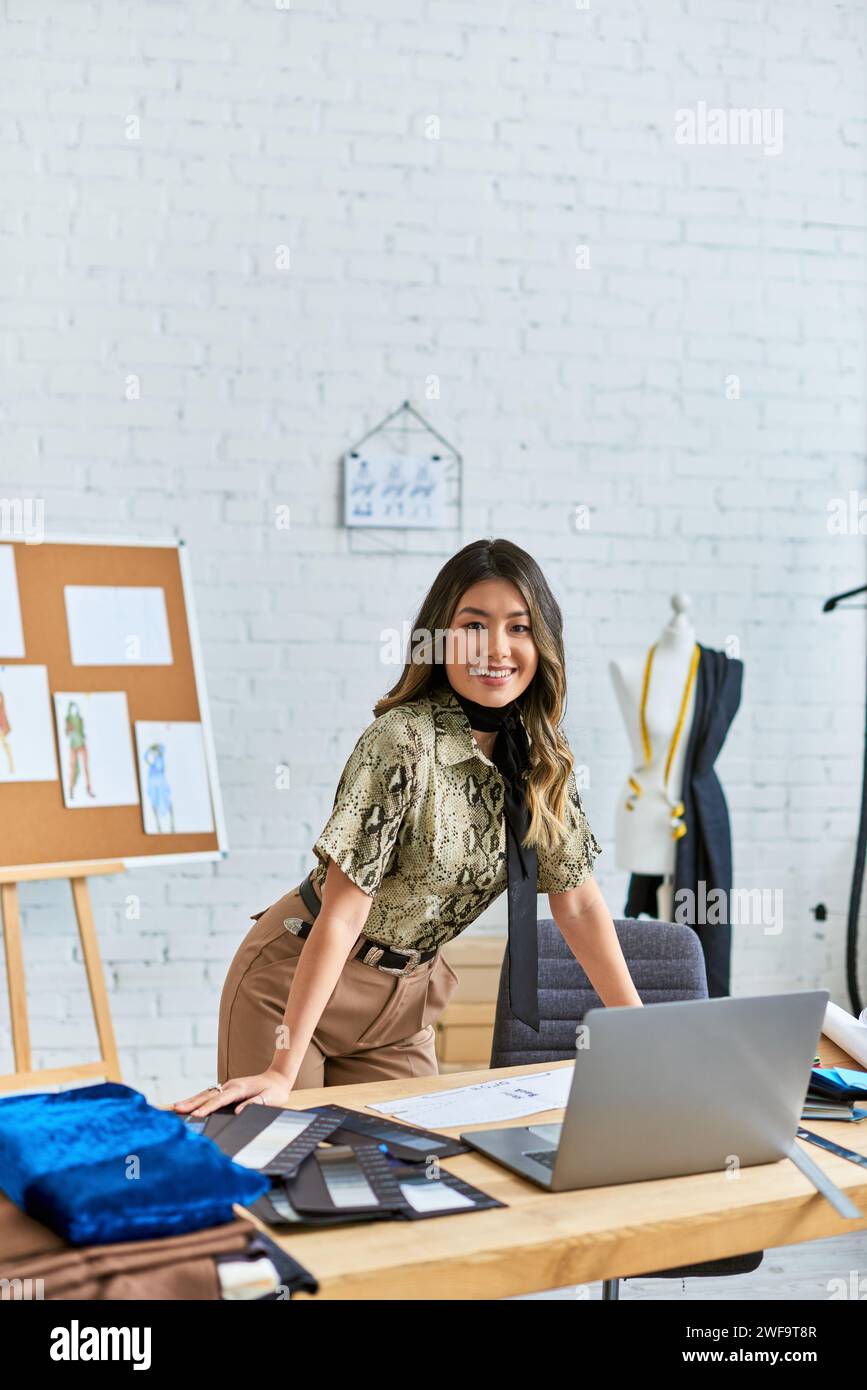 joyeuse styliste asiatique personnelle regardant la caméra au bureau de travail avec ordinateur portable dans l'atelier, petite entreprise Banque D'Images